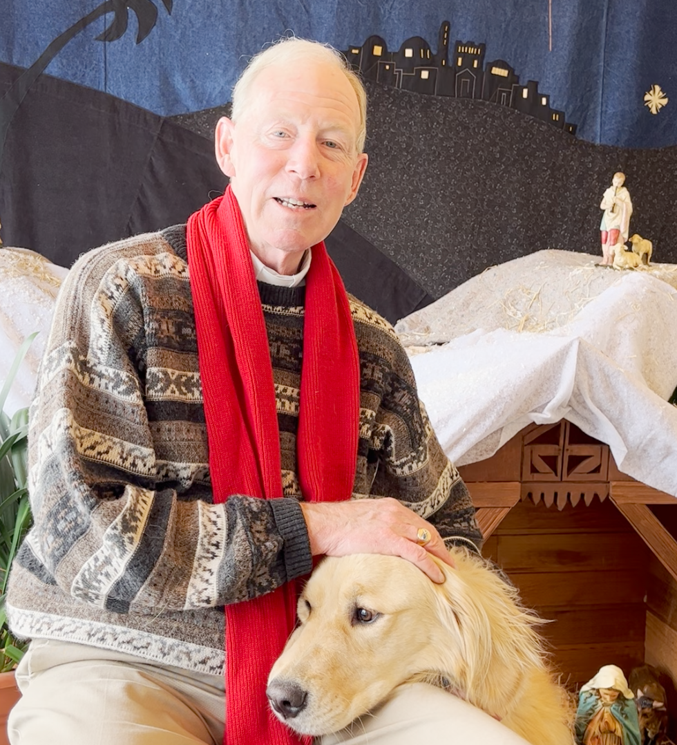 Bishop Gary Gordon and Taku the Golden Retreiver sitting in front of a creche