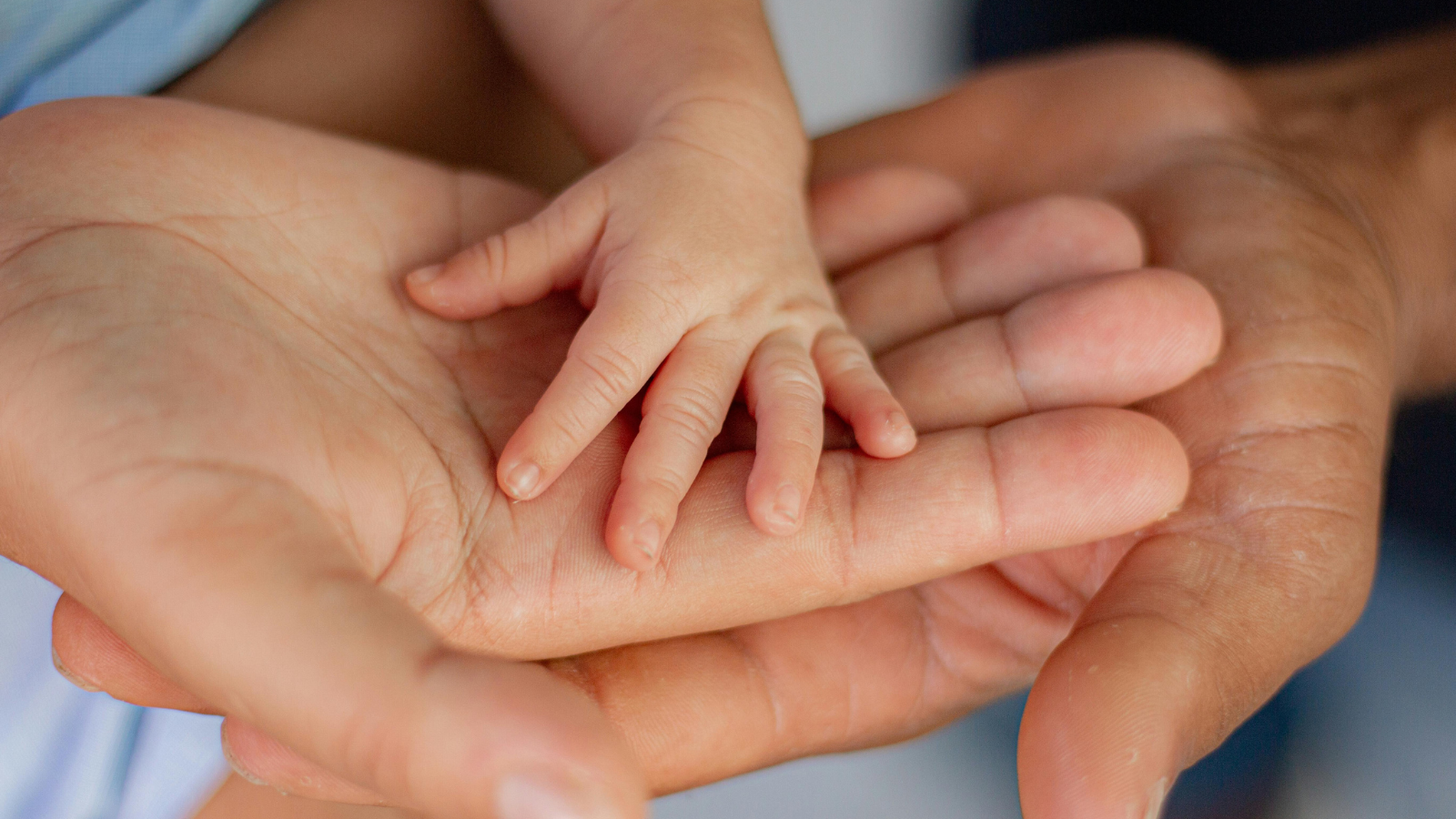 A close-up image of three hands—an adult's, a child's, and a baby's—gently placed on top of each other, symbolizing family, love, and generational connection.