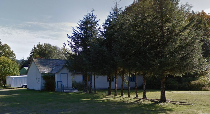 A small white building with trees in the foreground