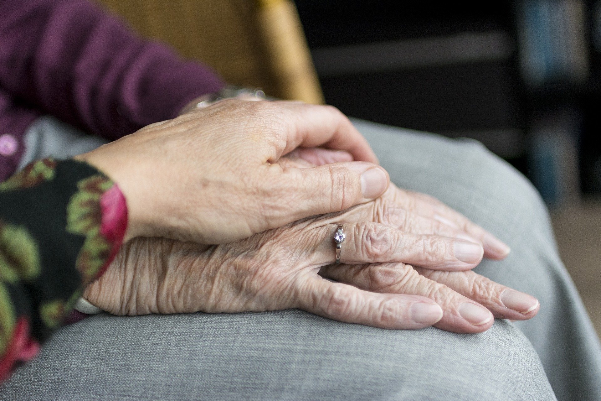 The hand of a younger person holds the hands of an older person